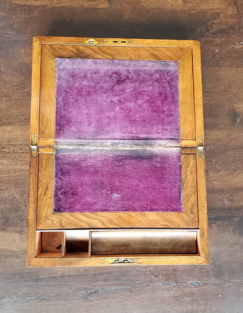 May include: A wooden writing desk with a hinged lid and a purple velvet interior. The desk has a small compartment with dividers and a long drawer.