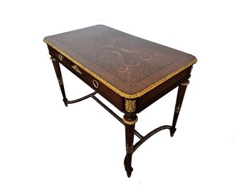 May include: A dark wood writing desk with a marquetry top and gold accents. The desk has a single drawer and four legs.
