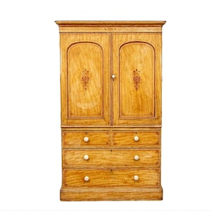 May include: A tall wooden cabinet with two doors and four drawers. The cabinet is made of light wood with a warm brown finish. The doors have a decorative design and the drawers have simple knobs.