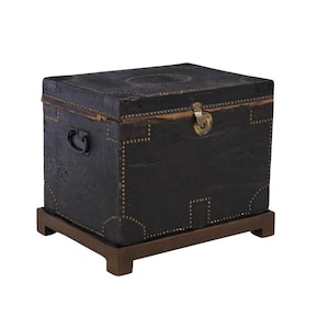 May include: A black leather-covered chest with brass hardware and a wooden base. The chest has a decorative pattern of brass studs around the edges.
