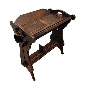 May include: A dark brown wooden table with a shelf and intricate carvings. The table has a rectangular top and is supported by two legs on each side.