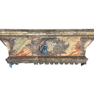 May include: An antique, rectangular wooden box with a painted religious scene. The box has a distressed, aged appearance with faded colors of blue, red, and gold. The box is likely a decorative or functional item.