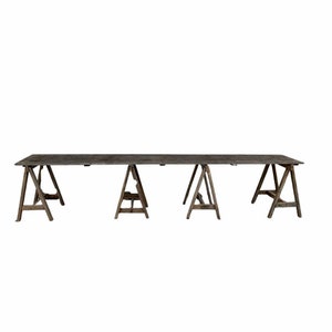 May include: A long wooden table supported by four wooden sawhorses. The table is made of dark wood and has a rustic look.
