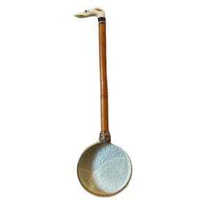 May include: A wooden ladle with a white dog head handle. The ladle is made of metal and has a round bowl.