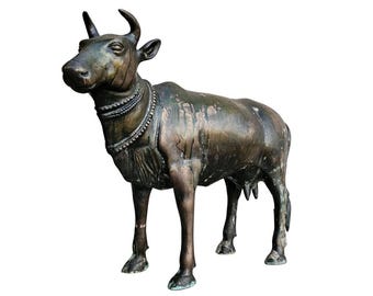 Puede incluir: Una estatua de bronce de una vaca con un collar decorativo. La estatua está de pie sobre un fondo blanco.