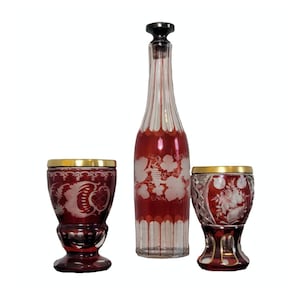 May include: A set of three ruby red glass decanter and two glasses with etched floral designs. The decanter has a silver stopper.