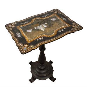 May include: A small, black, rectangular table with a decorative top made of inlaid mother-of-pearl and gold. The table has a single, turned wooden leg and a four-pronged base.