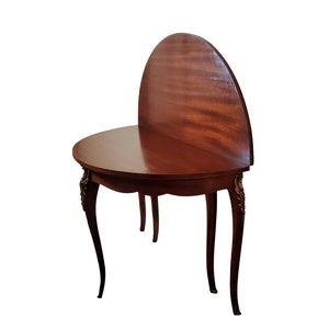 May include: A dark wood, half-round table with ornate legs and a drop leaf. The table is closed and the leaf is raised.