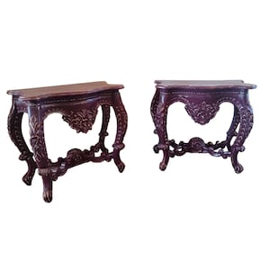 May include: Two ornate, dark brown side tables with carved details. Each table has a curved top, decorative legs, and a central floral design. The tables are approximately 30 inches long.