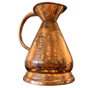 May include: A copper pitcher with a wide mouth and a handle. The pitcher has a hammered finish and a slightly tarnished appearance.