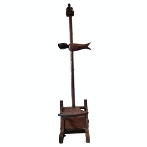 May include: A wooden stand with a carved figure at the top and a carved fish fin on the side. The stand has a seat and a tall, thin pole.