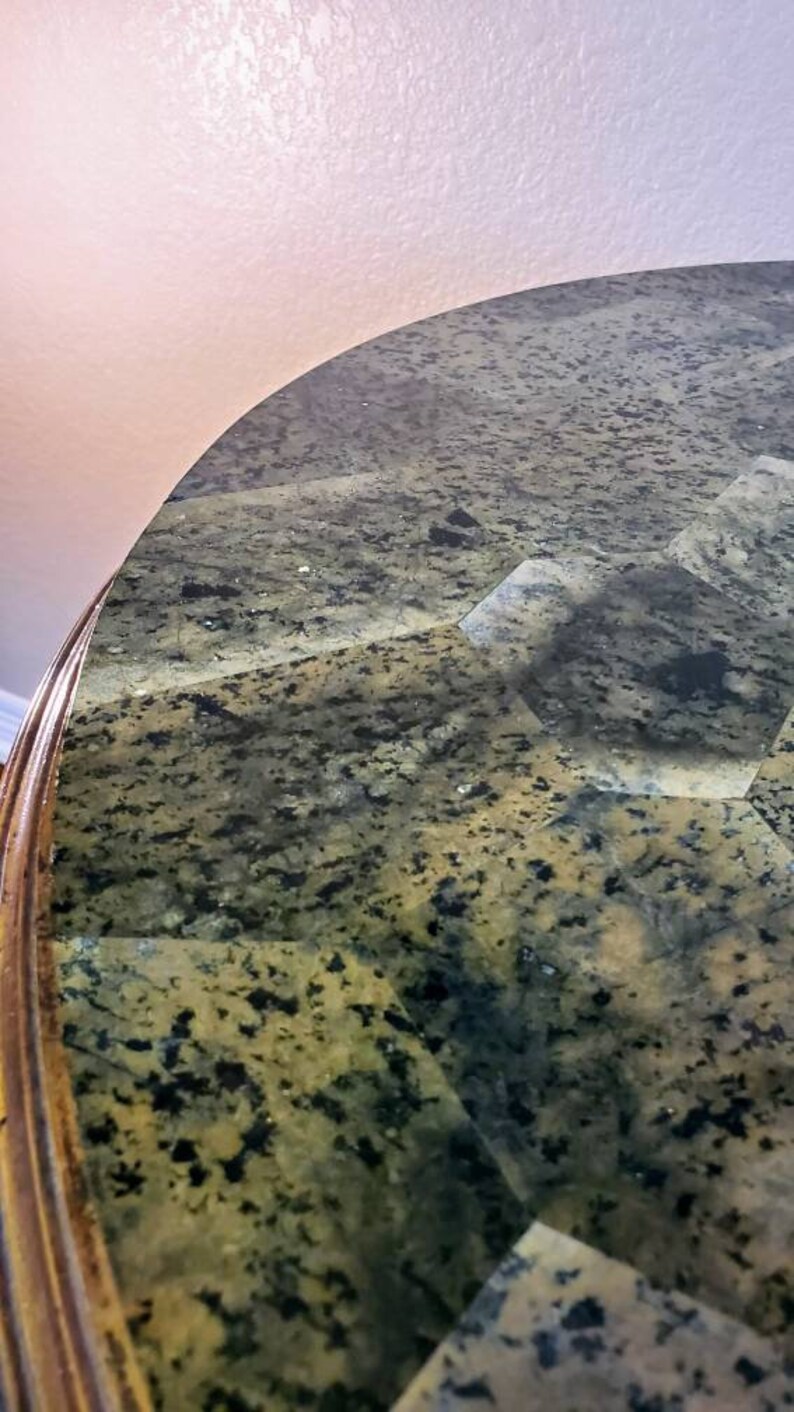 May include: Close-up of a table with a patterned granite top. The surface is a mix of green, black, and gray, with a polished finish. The table's edge is a warm, golden brown.