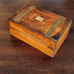 May include: A wooden box with brass accents. The box has a hinged lid and a brass plate on the top.