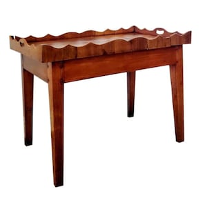 May include: A wooden table with a scalloped edge and four tapered legs. The table is made of a warm-toned wood and has a rectangular top with a decorative edge. The legs are angled and provide stability to the table.