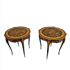 May include: A pair of round, wooden end tables with intricate marquetry inlays. The tables have a dark wood finish and gold accents. The inlays feature floral and geometric patterns.