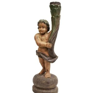 May include: A wooden statue of a cherub holding a green and brown torch. The statue is standing on a round wooden base.