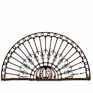 May include: A large, rusty metal archway with a decorative design. The archway is made of metal bars that are arranged in a fan shape. The archway has a decorative design at the bottom that includes the letters "L.S.D."