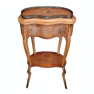 May include: A small, oval-shaped, wooden table with intricate marquetry inlay. The table has a single drawer and a shelf. The legs are curved and have a decorative design. The table is made of light wood with a dark brown stain.