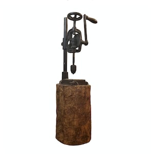 May include: A vintage cast iron hand drill press mounted on a wooden base. The drill press has a crank handle and a metal drill bit.