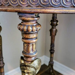 May include: Ornate antique table with a marble top and detailed carvings. The table features a bronze bust of a woman and decorative brass accents. The legs are intricately designed with classical motifs, showcasing a blend of materials and craftsmanship.