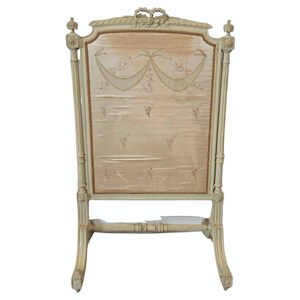 May include: A white painted wooden fire screen with a delicate floral design on the fabric panel. The screen has a curved top and a base with scrolled legs.