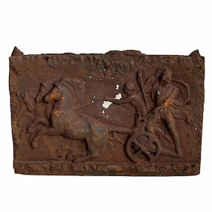 May include: A rusty metal plaque with a raised relief sculpture of a chariot pulled by two horses. Two figures are depicted in the chariot, one holding reins and the other holding a spear.