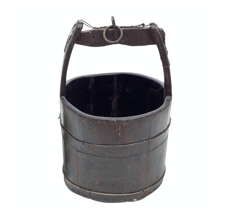 Puede incluir: Un cubo de madera marr&oacute;n oscuro con un asa de metal. El cubo tiene una cuerda envuelta alrededor de la parte superior y un anillo de metal en el asa.