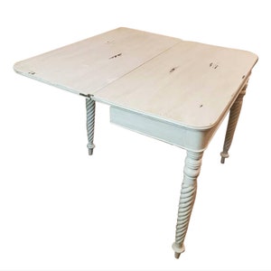 May include: White painted drop leaf table with turned legs. The table top is made of wood and has a distressed finish.