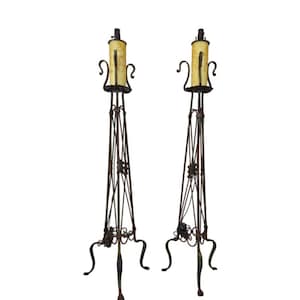 May include: A pair of tall, wrought iron floor lamps with a decorative, geometric design. Each lamp has a yellow, frosted glass shade.