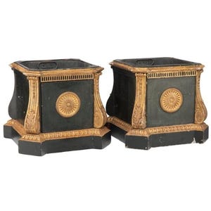May include: Two matching black and gold decorative boxes. Each box has a square shape with a gold trim and a circular gold design on the front. The boxes have a pedestal base and are likely used for storage or display.