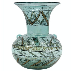 May include: A turquoise glass vase with gold and black painted designs. The vase has a wide mouth and a round body with two handles.