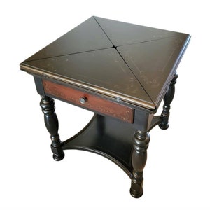 May include: A black wooden table with a lift-top and a drawer. The table has a decorative design on the top and legs. The table is in the closed position.