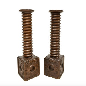 May include: A pair of wooden candle holders with a unique screw design. The holders are carved with grapevine motifs and have a dark brown finish.