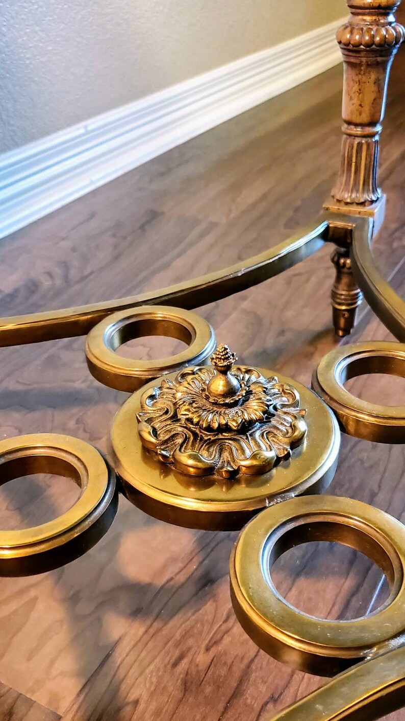 May include: A close-up of a gold-toned, ornate coffee table. The table features a glass top with decorative gold rings and a central, detailed medallion. The legs and frame are also gold, creating a cohesive, elegant design.