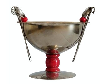 May include: A silver bowl with two red handles and a red base. The bowl is on a white background.