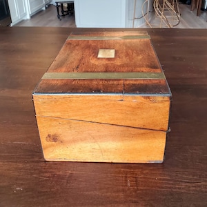 May include: A wooden writing box with brass accents. The box is closed and has a slanted top.