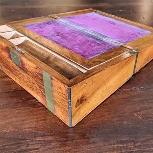 May include: A wooden writing box with a purple velvet interior and brass accents. The box has a hinged lid and a compartment for writing supplies.