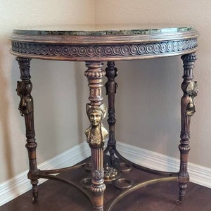 May include: An antique, round side table with a green marble top and ornate, carved wooden legs. The legs feature decorative brass accents and are supported by a brass base. The table is approximately 30 inches in diameter.