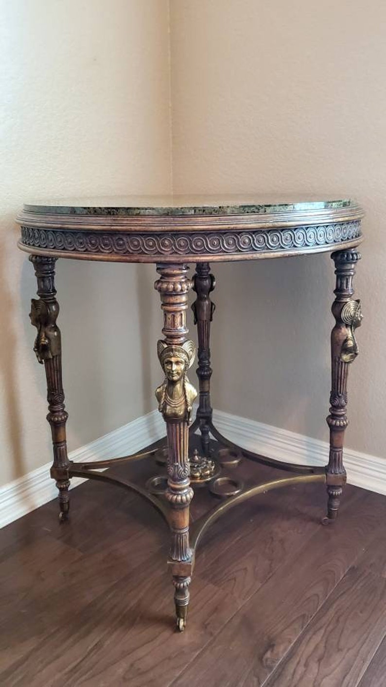May include: An antique, round side table with a green marble top and ornate, carved wooden legs. The legs feature decorative brass accents and are supported by a brass base. The table is approximately 30 inches in diameter.