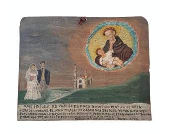 May include: A hand-painted wooden plaque depicting Saint Anthony of Padua holding a baby Jesus. The plaque also features a wedding couple and a church in the background. The text on the plaque reads "SAN ANTONIO DE PADUA ES PARA NOSOTROS MOTIVO DE GRAM AGRAMESIMIENTO. EL GONTO MILAGRO DE CASARNOS DESPUES DE TANTO TIEMPO PUES AMBOS ERAMOS NOVIOS DE OTRAS PERSONAS PERO ESTABAMOS ENAMORADOS Mos YCADA UNO POR SULADO TE PIDIO EL MILAGRITO Y TU LAS CONCEDIDOP RACIELITA'Y BERNARDO KIANGA PUEBLA 2948."