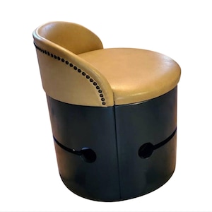 May include: A round, black, wooden stool with a tan leather seat and a decorative nailhead trim. The stool has a unique design with two cutouts on the side.