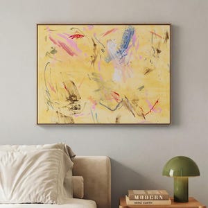 May include: Abstract art piece with a yellow background and colorful brushstrokes in pink, blue, and red. The artwork is framed in a thin, dark brown frame and hangs on a light gray wall. A bed with white linens and a nightstand with a green lamp are in the foreground.