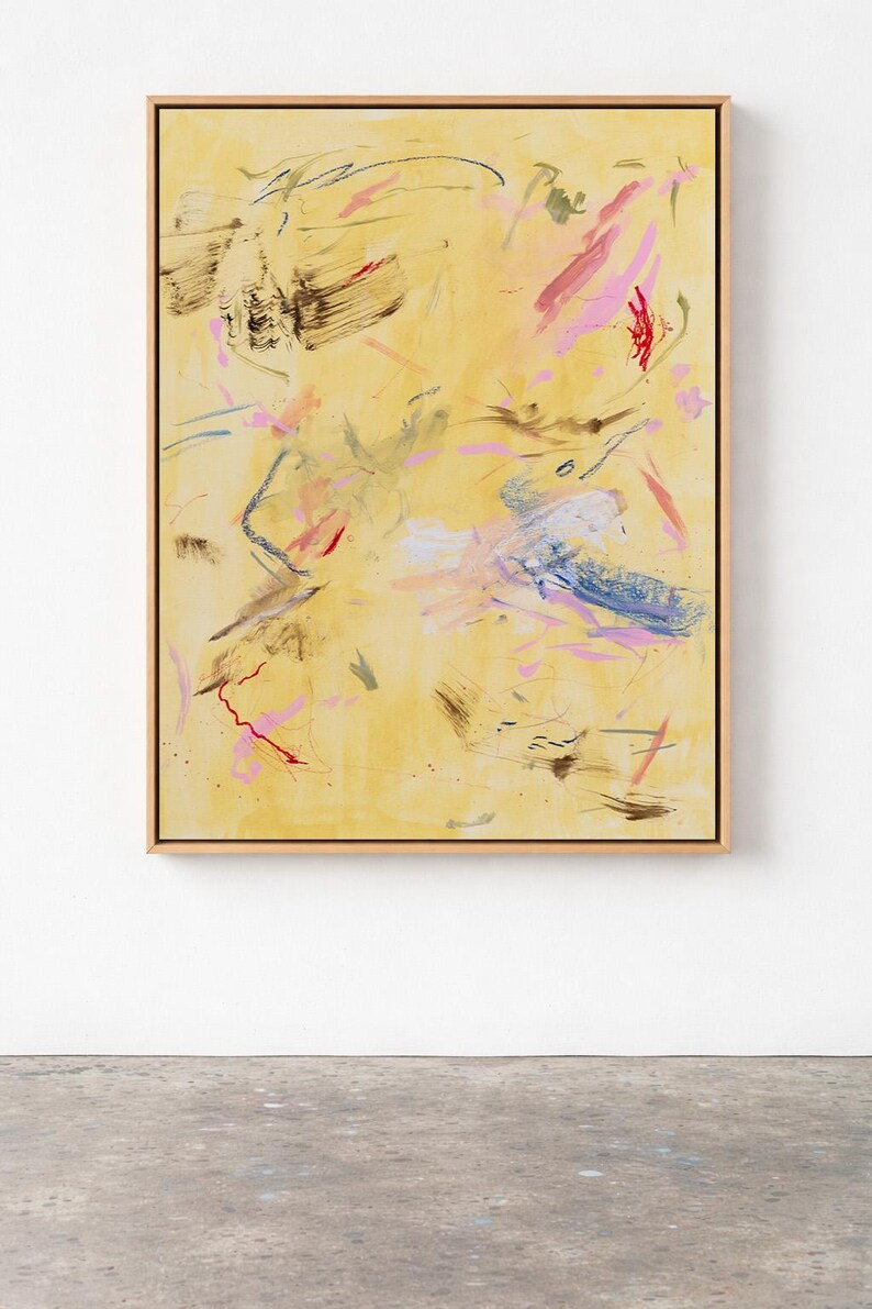 May include: Abstract painting on canvas with a light yellow background. The artwork features brushstrokes in shades of pink, blue, red, and brown. The painting is framed in a light wood frame and is displayed against a white wall.
