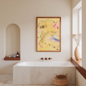 May include: Abstract art piece in a wooden frame. The artwork features a yellow background with brushstrokes of pink, blue, and black. The painting hangs above a white bathtub in a bathroom setting. A woven basket sits on the floor.