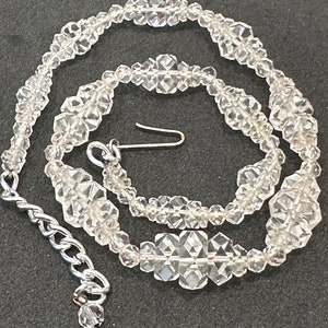 May include: A clear crystal necklace with a silver clasp. The necklace is made of faceted beads that are strung together in a repeating pattern.