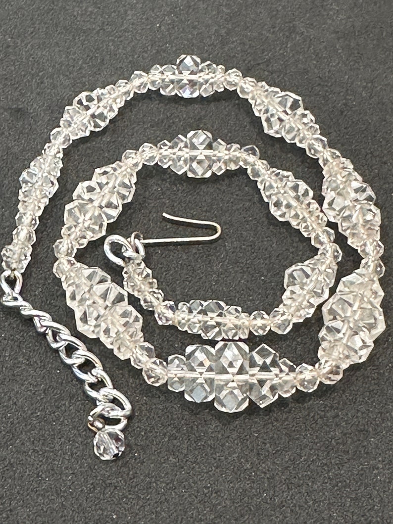 May include: A clear crystal necklace with a silver clasp. The necklace is made of faceted beads that are strung together in a repeating pattern.