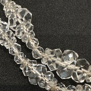 May include: A close-up of a strand of clear crystal beads. The beads are faceted and have a geometric shape. The beads are strung on a clear thread.
