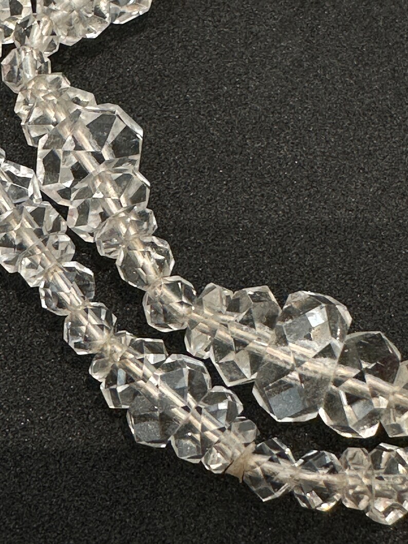 May include: A close-up of a strand of clear crystal beads. The beads are faceted and have a geometric shape. The beads are strung on a clear thread.