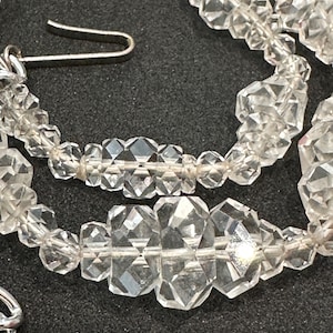 May include: A close-up of a crystal necklace with faceted beads. The necklace is made of clear quartz crystals and has a silver clasp.