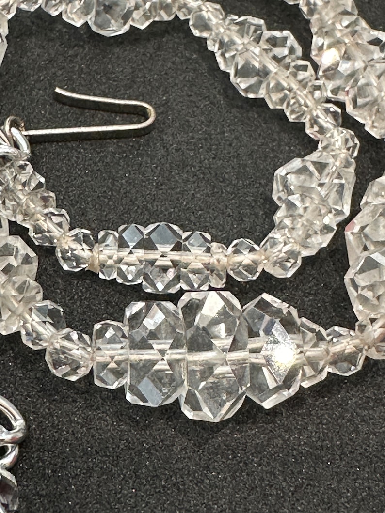 May include: A close-up of a crystal necklace with faceted beads. The necklace is made of clear quartz crystals and has a silver clasp.